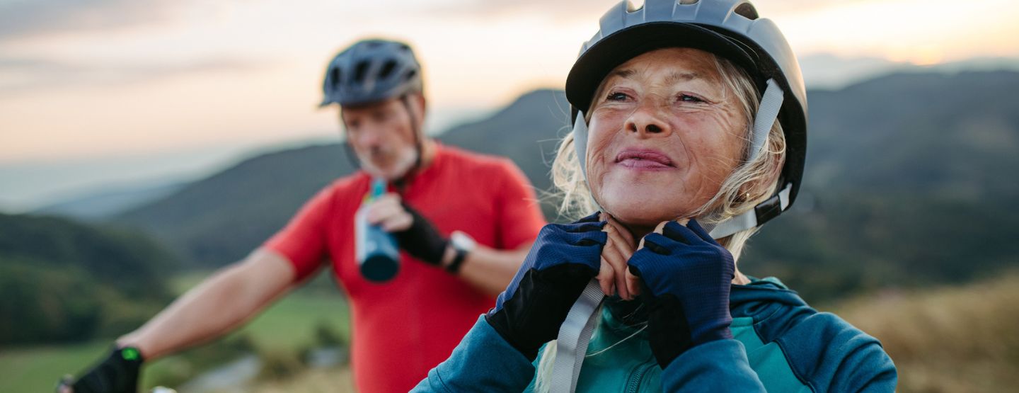 Mature woman straps helmet on in preparation for mountain bike ride.