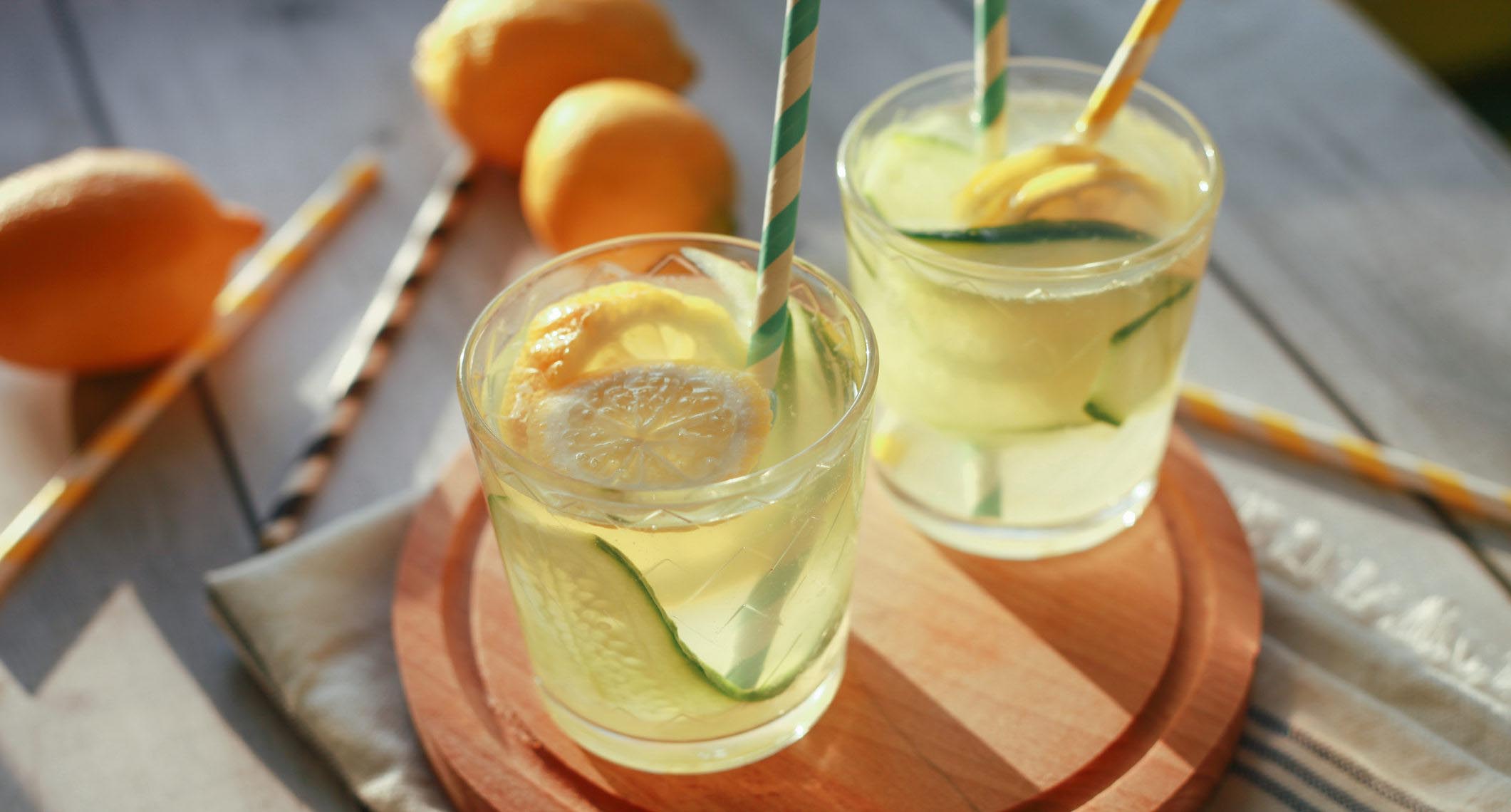 Glass of homemade lemonade made of lemon and cucumber with paper drinking straws.