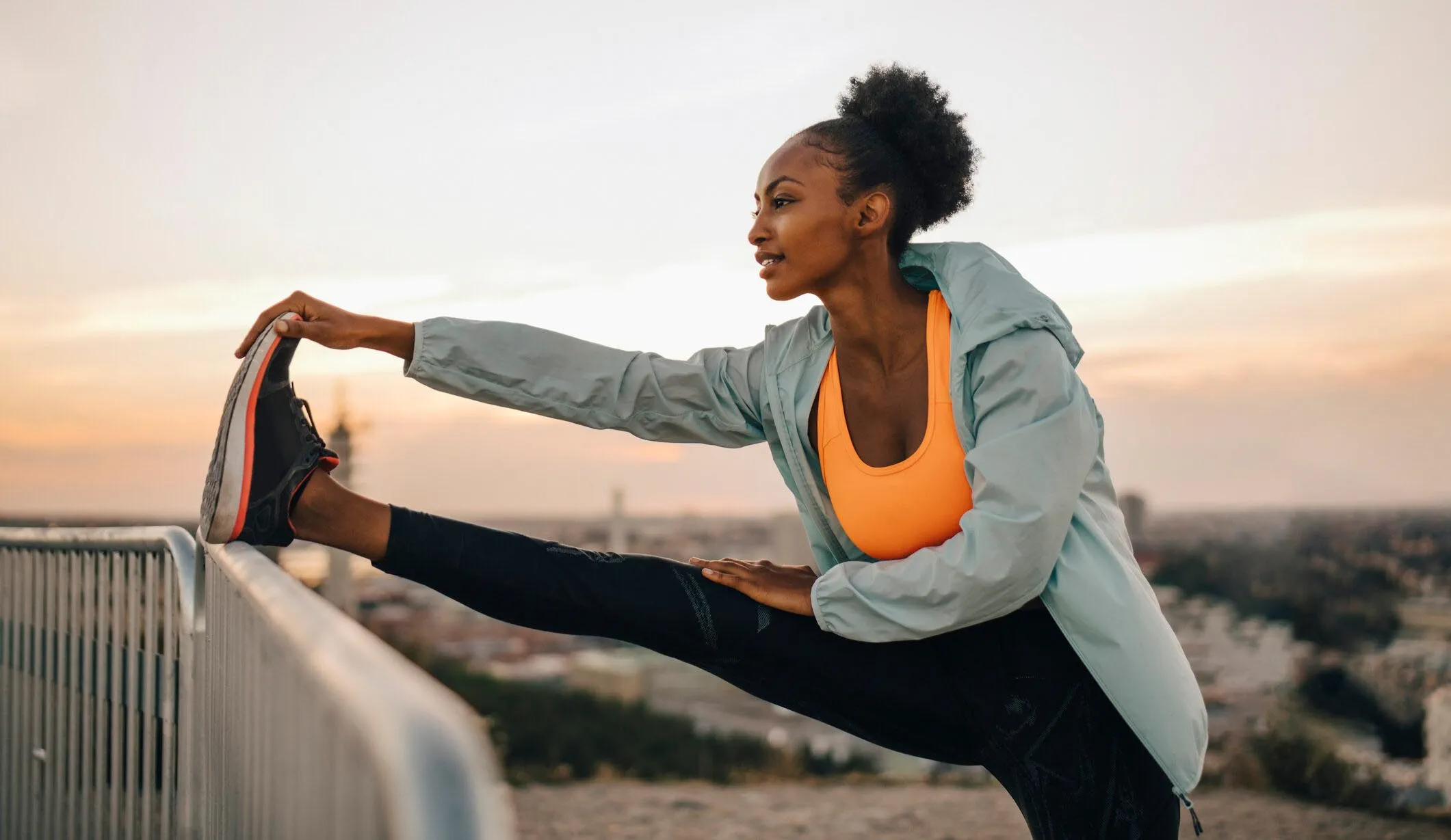 An athletic woman stretches her leg on a railing before going jogging.
