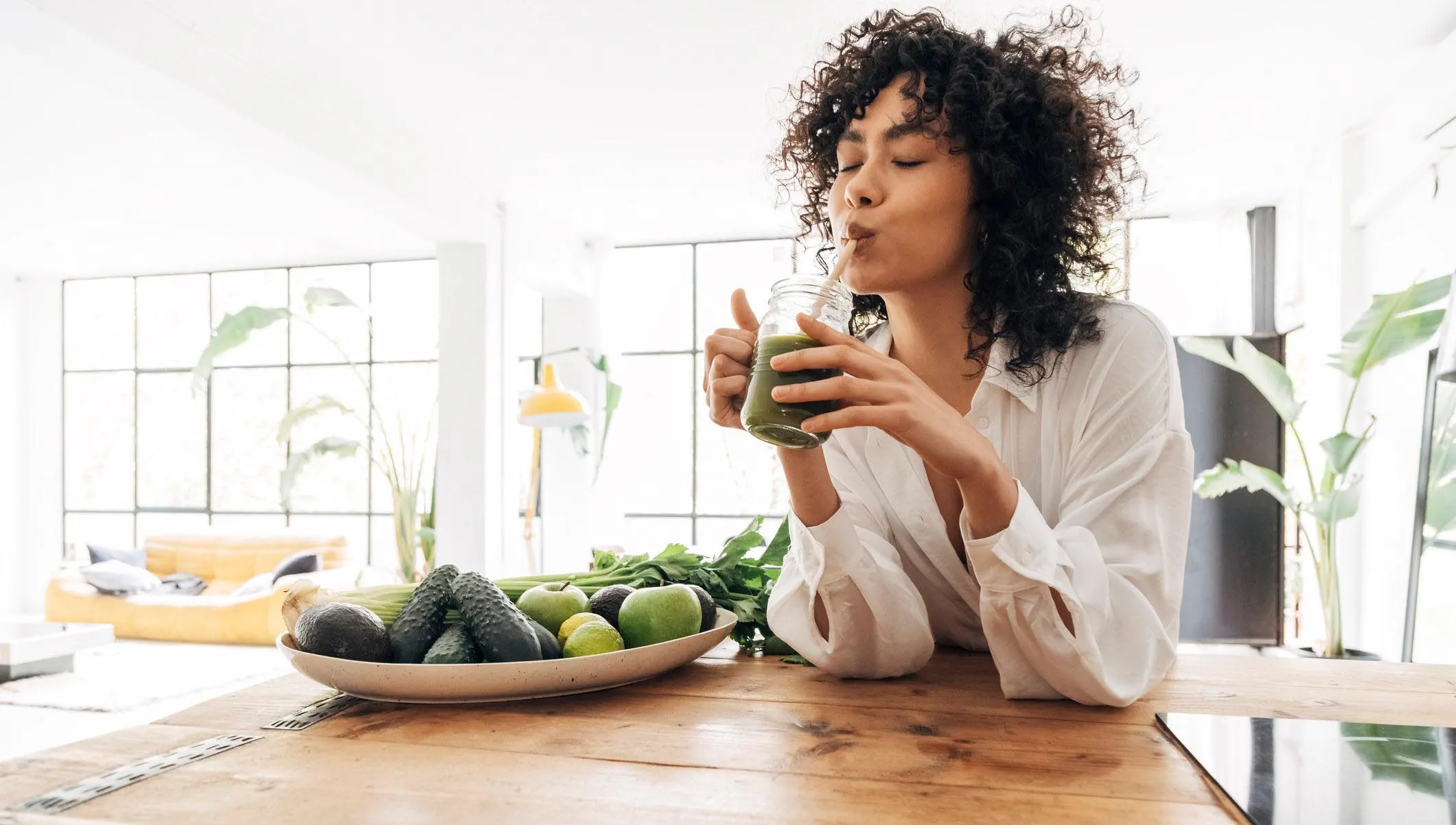 Young African American woman drinking green juice with reusable bamboo straw in loft apartment.