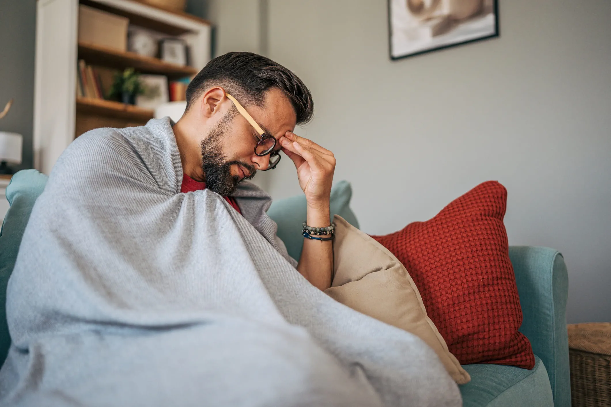 Man sitting on the couch, touching his forehead with his eyes closed