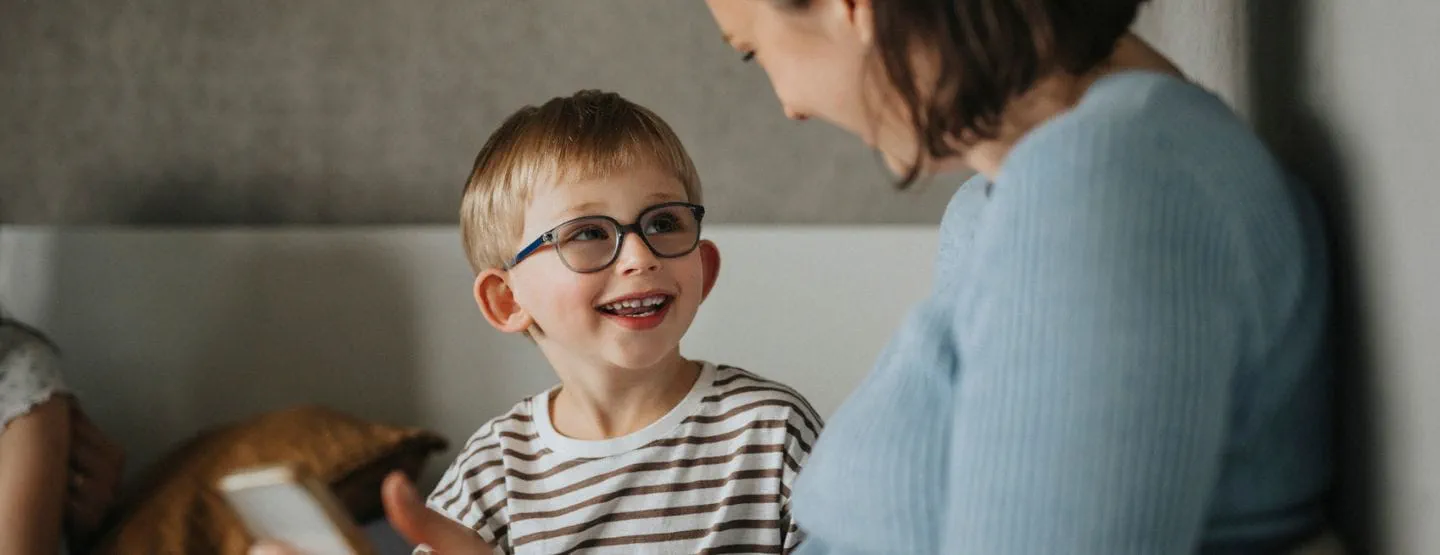 Child wearing glasses smiles at mom.