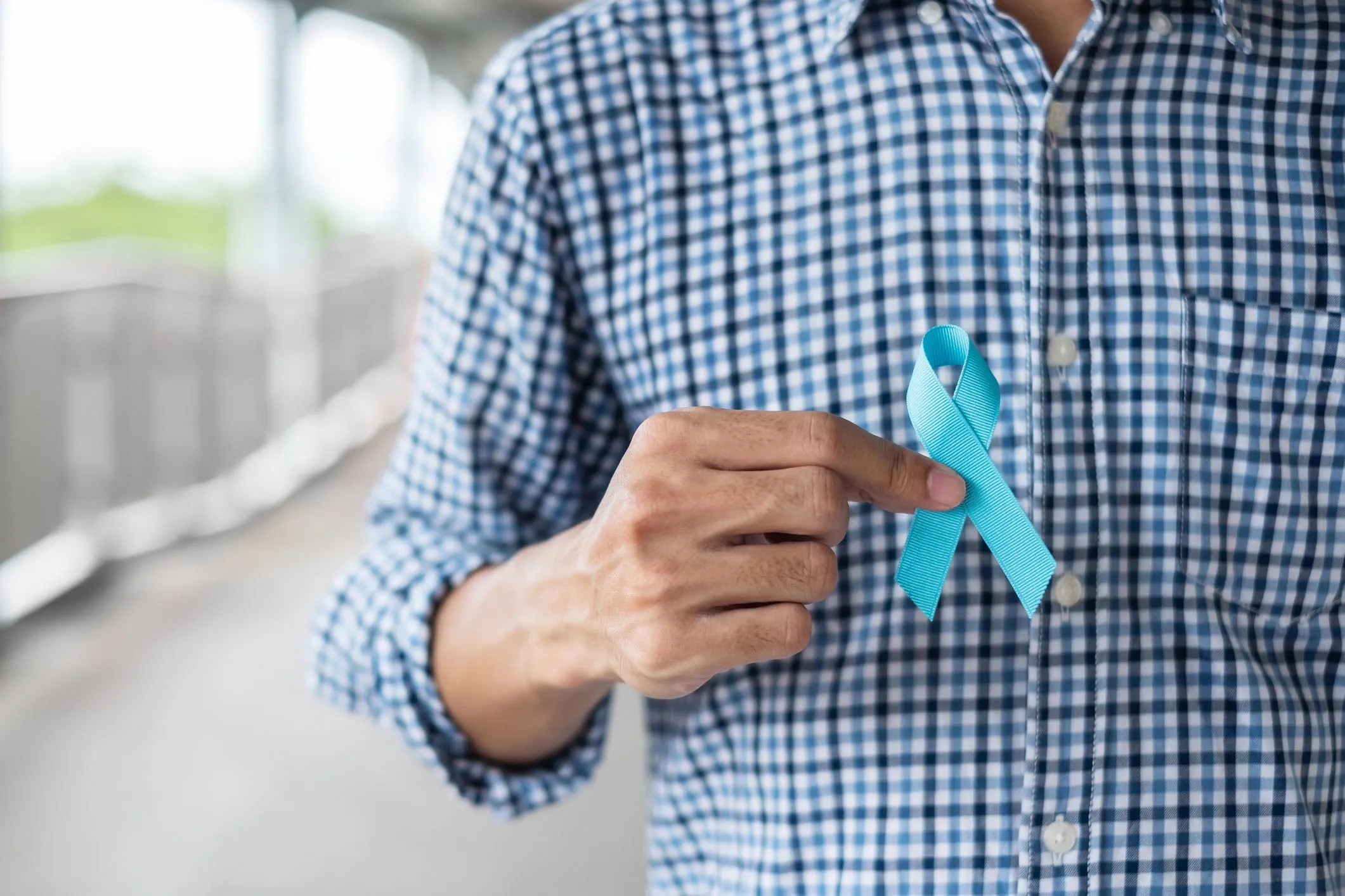 Man in blue shirt with hand holding Blue Ribbon for supporting people living and illness.