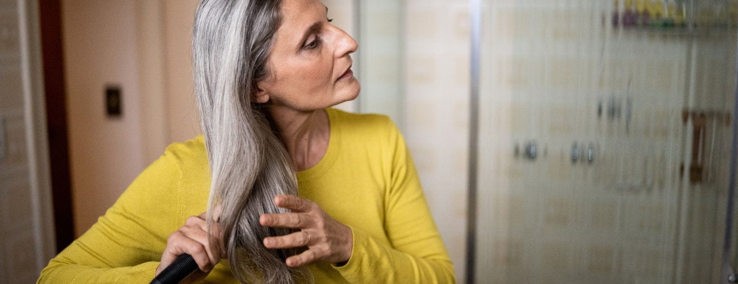 Middle-aged woman brushing hair in bathroom.