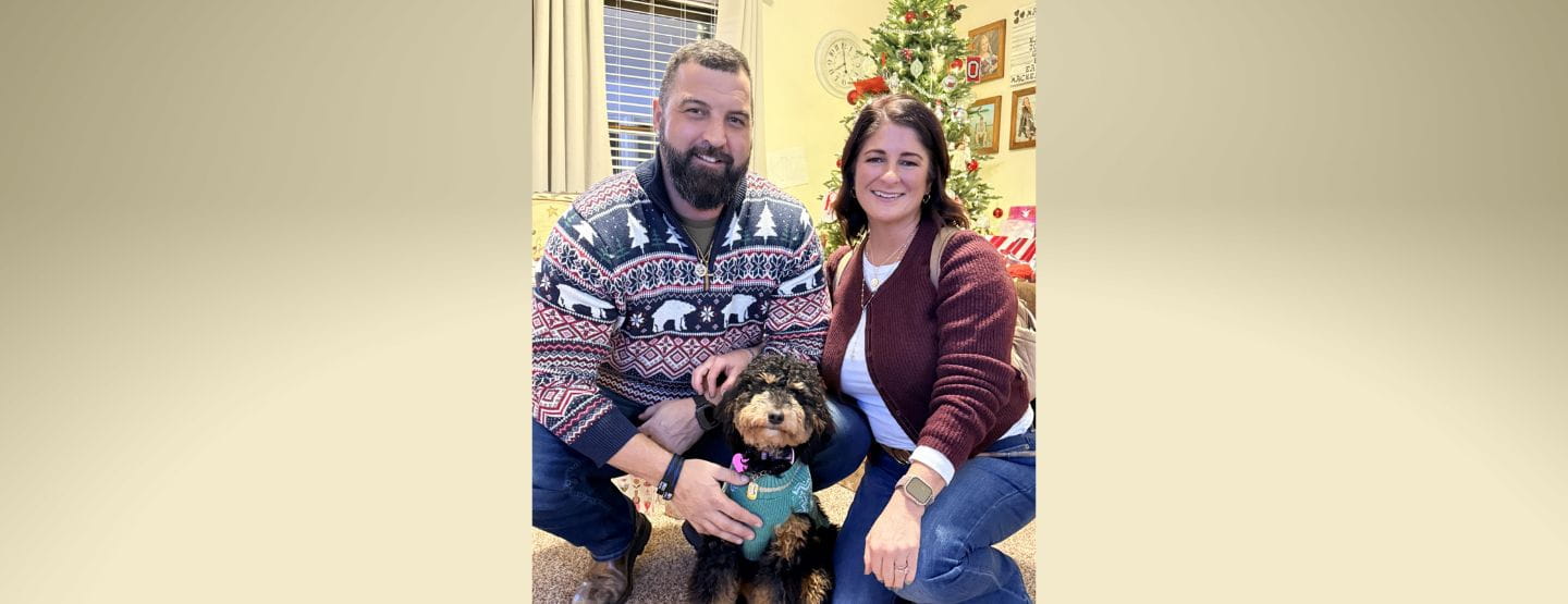 Stacey Mack smiles at the camera with husband and dog. 