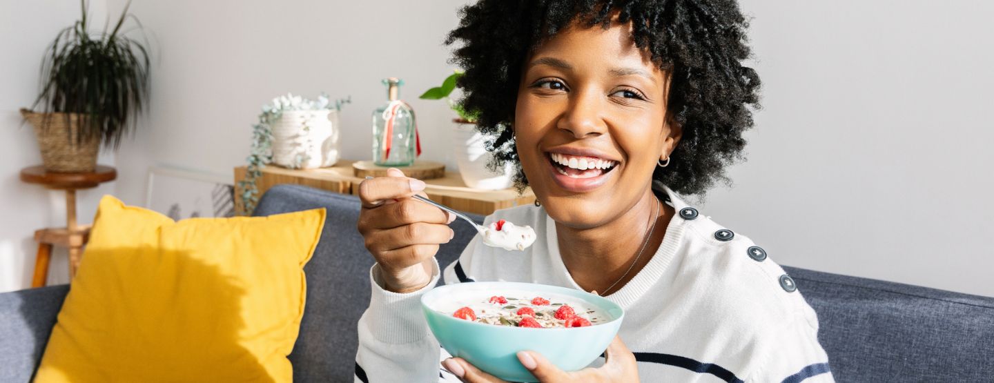 Young woman smiling while eating a bowl of yogurt while sitting on the couch.