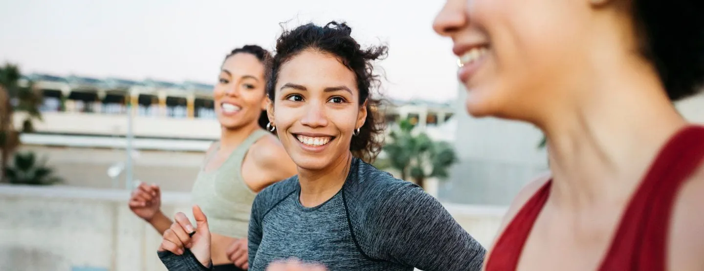 Three women smiling while on a run outside.