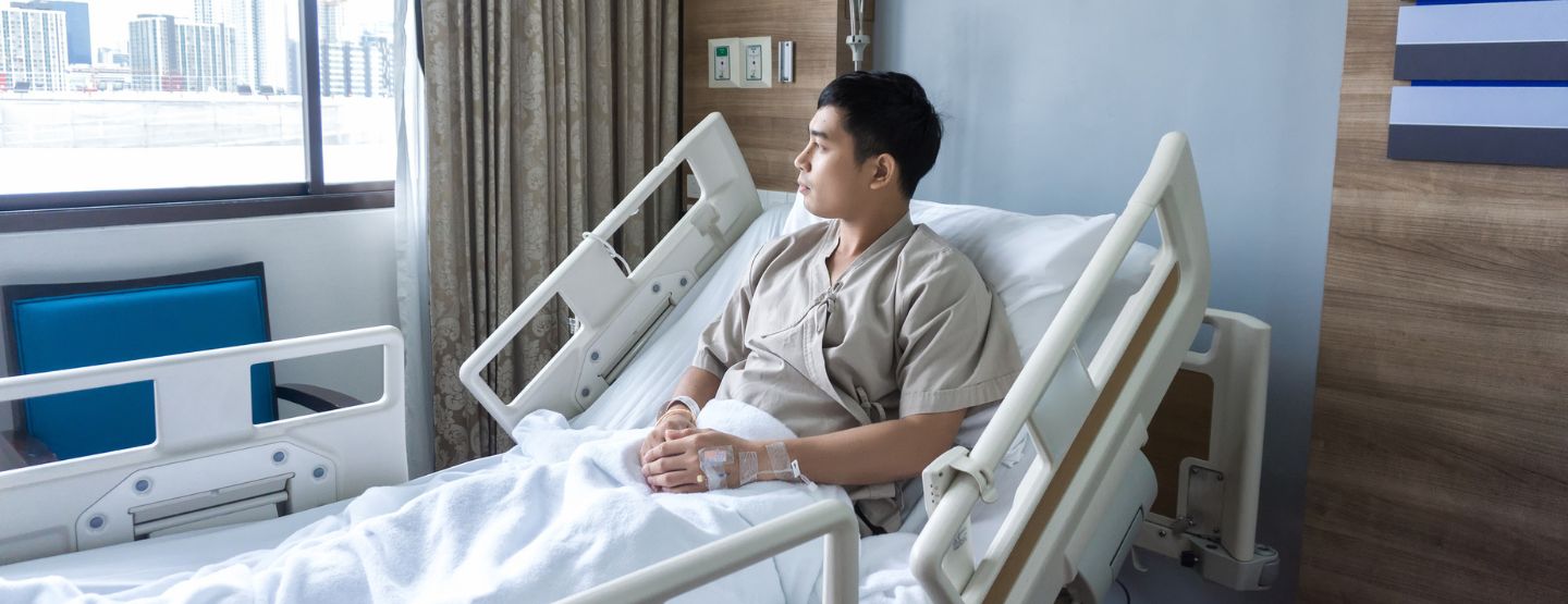 Young man sitting in hospital bed looking out the window.