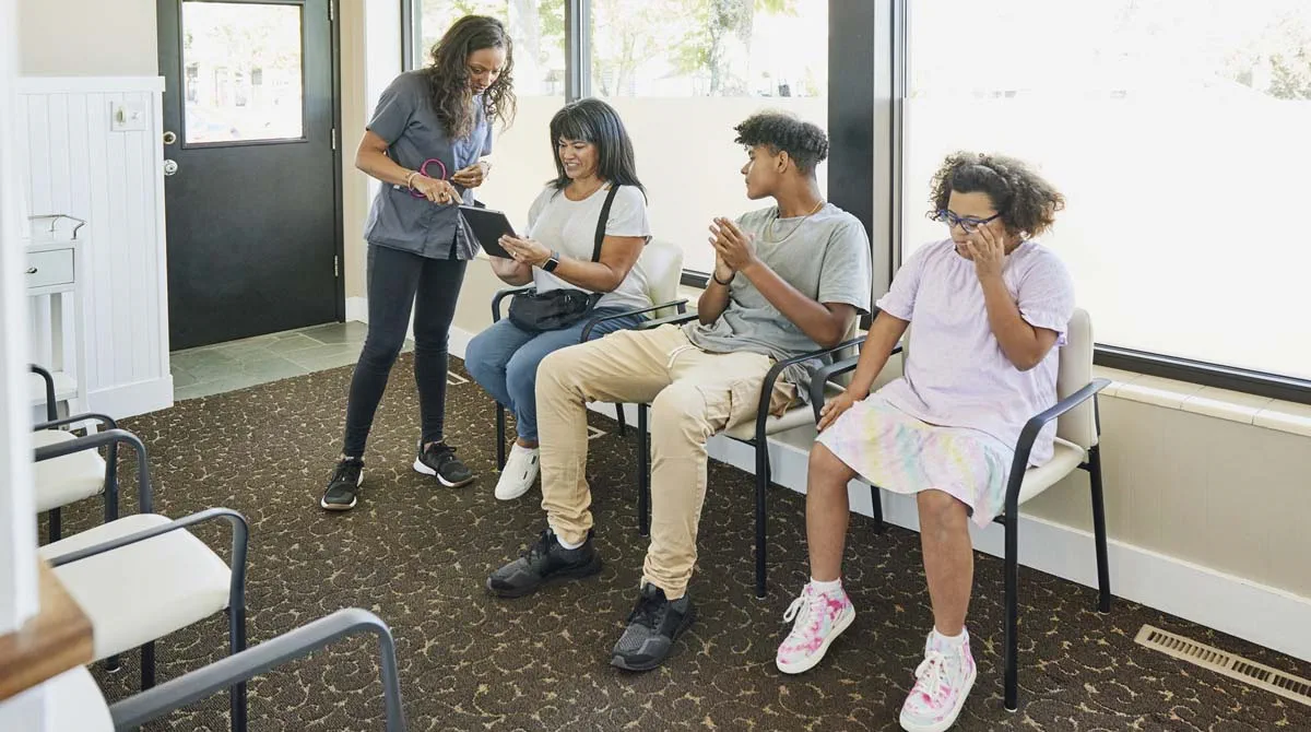 a family speaks to a dental receptionist in a waiting room 