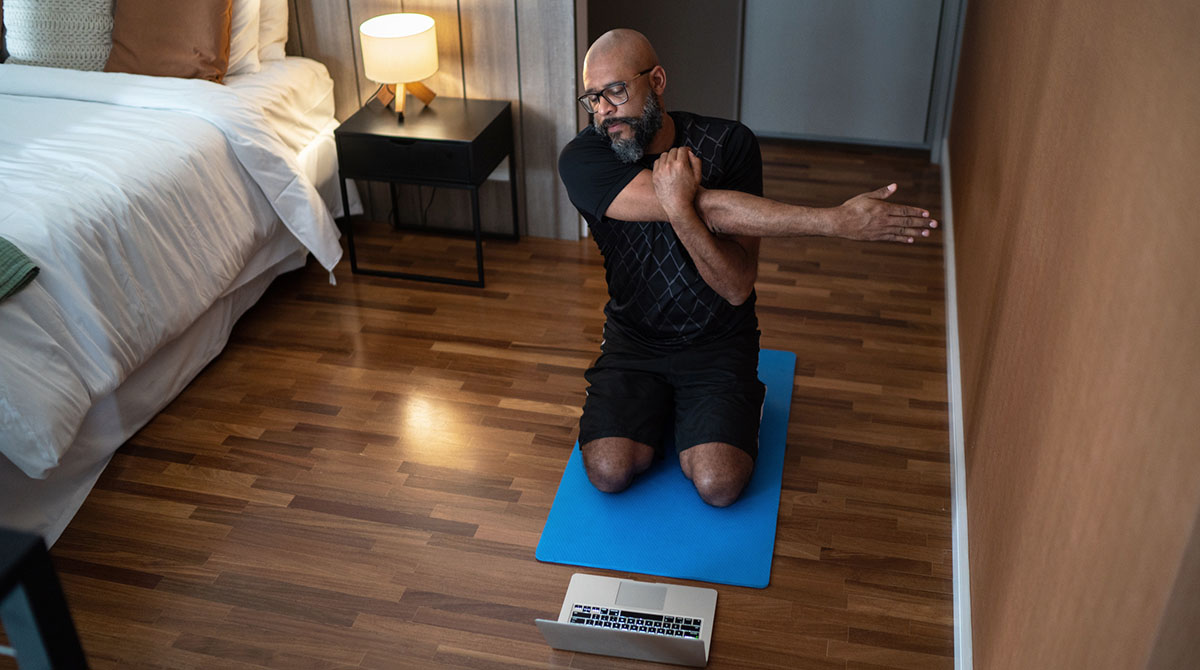 a man exercises at home using his laptop to view a workout online