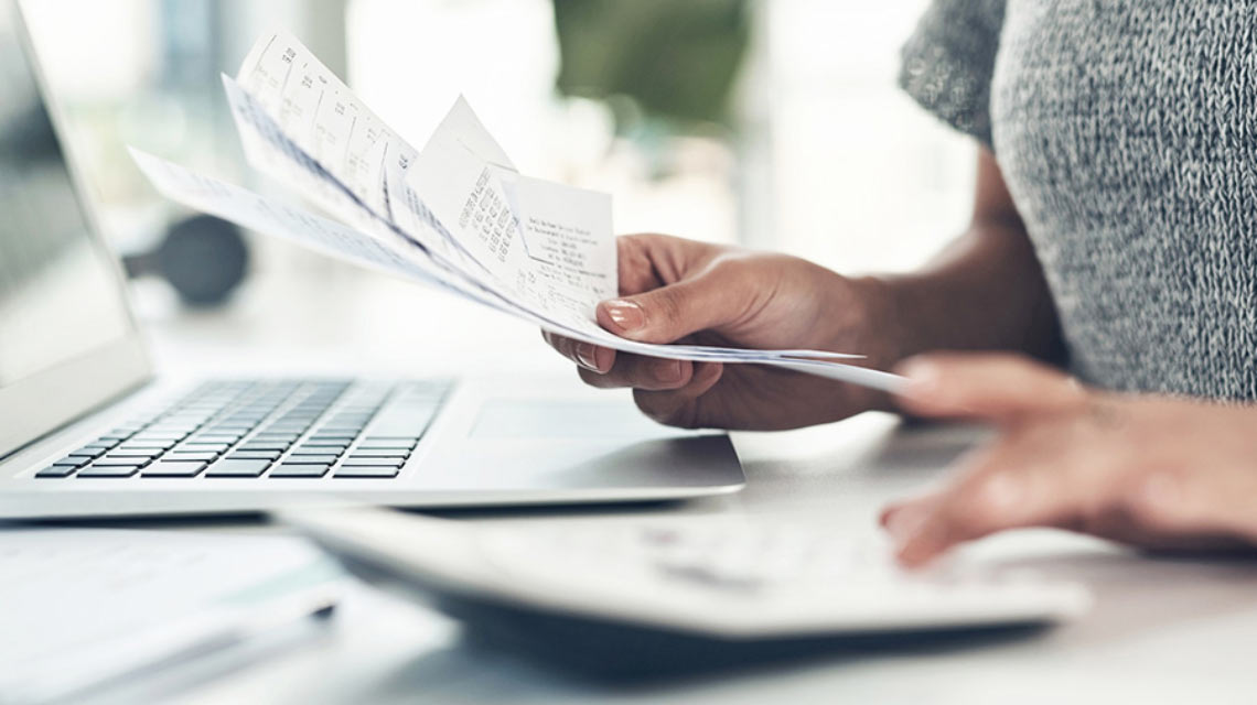 A woman's hands at her laptop, organizing receipts and reading the ProMedica Ebeid Newsletter