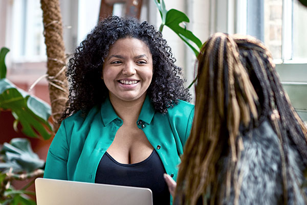 Two young women sit and speak in a casual work environment