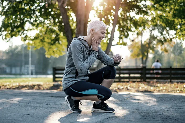 A mature woman bends down during a morning jog to check the pulse on her neck
