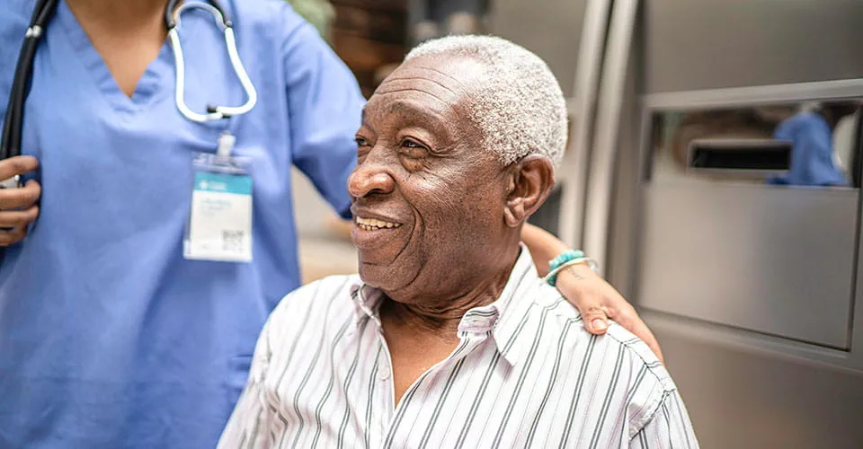 An elderman smiles as a nurse places her hand on his shoulder