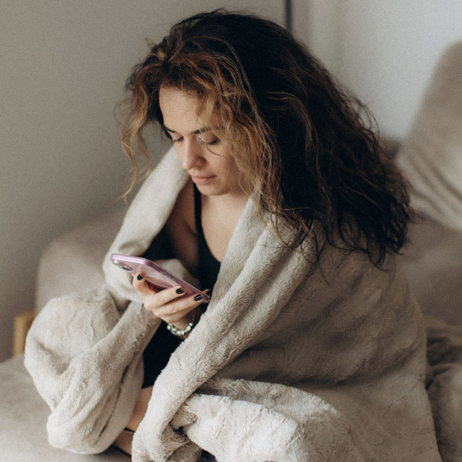 a young woman wrapped in a blanket uses her phone