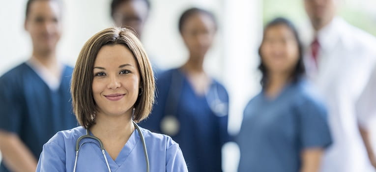 A smiling female nurse in the foreground with other nurses slightly out of focus in the background
