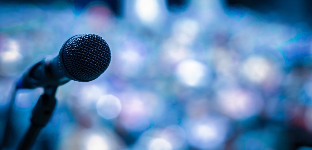 A microphone on a mic stand with a blurred out audience with lights.