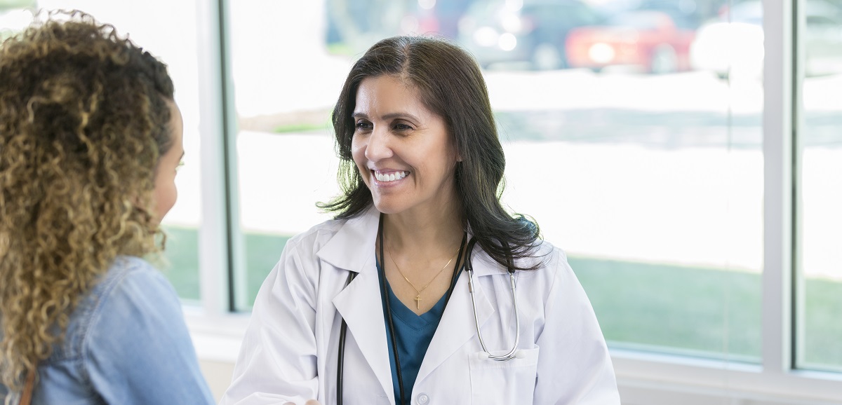 Confident mature Hispanic female doctor warmly greets a new female patient. They are shaking hands and are smiling at one another.