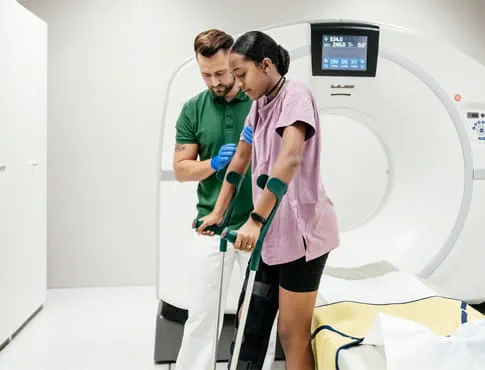a CT technician helps a patient stand with crutches