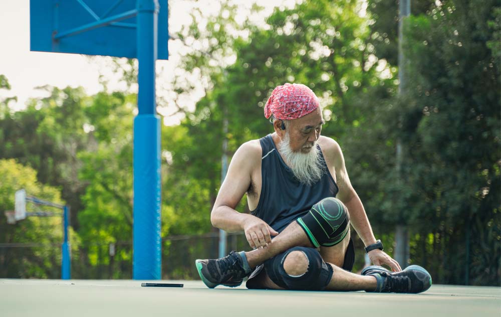 a senior man wearing a knee brace stretches his legs during an outdoor workout